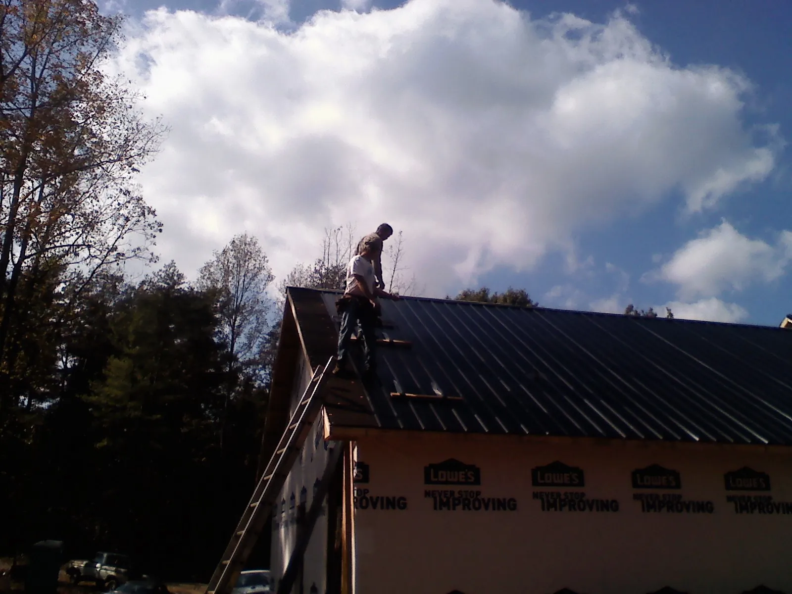 Roofer fastening dark metal panels high against a cloudy sky, from a Roof Inspection job in Marysville